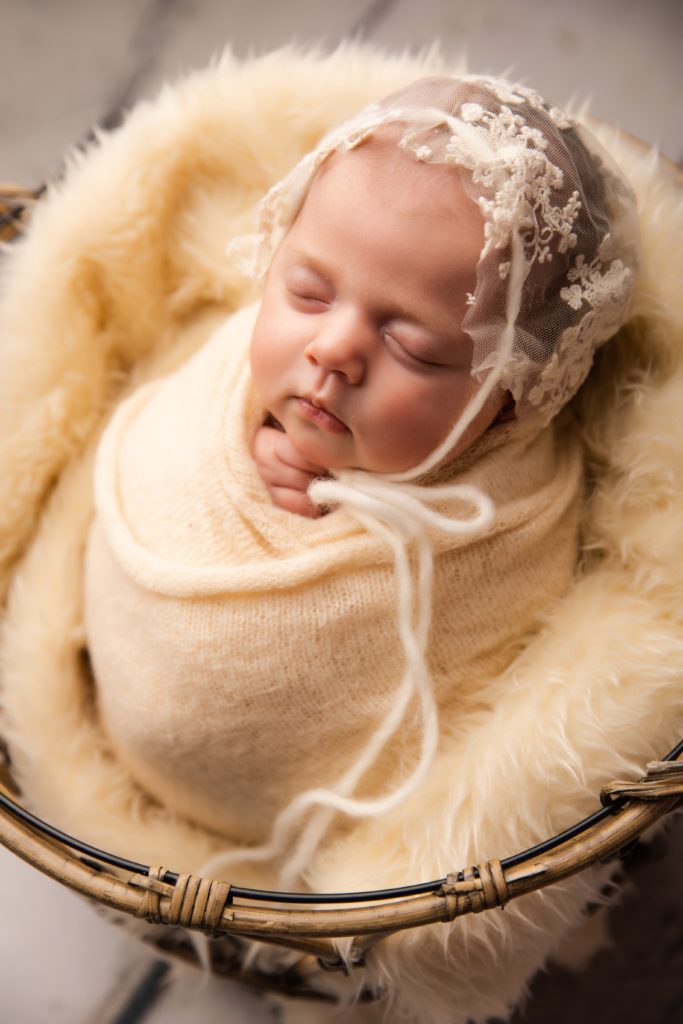 baby girl wearing a bonnet in basket surrounded by ivory fur